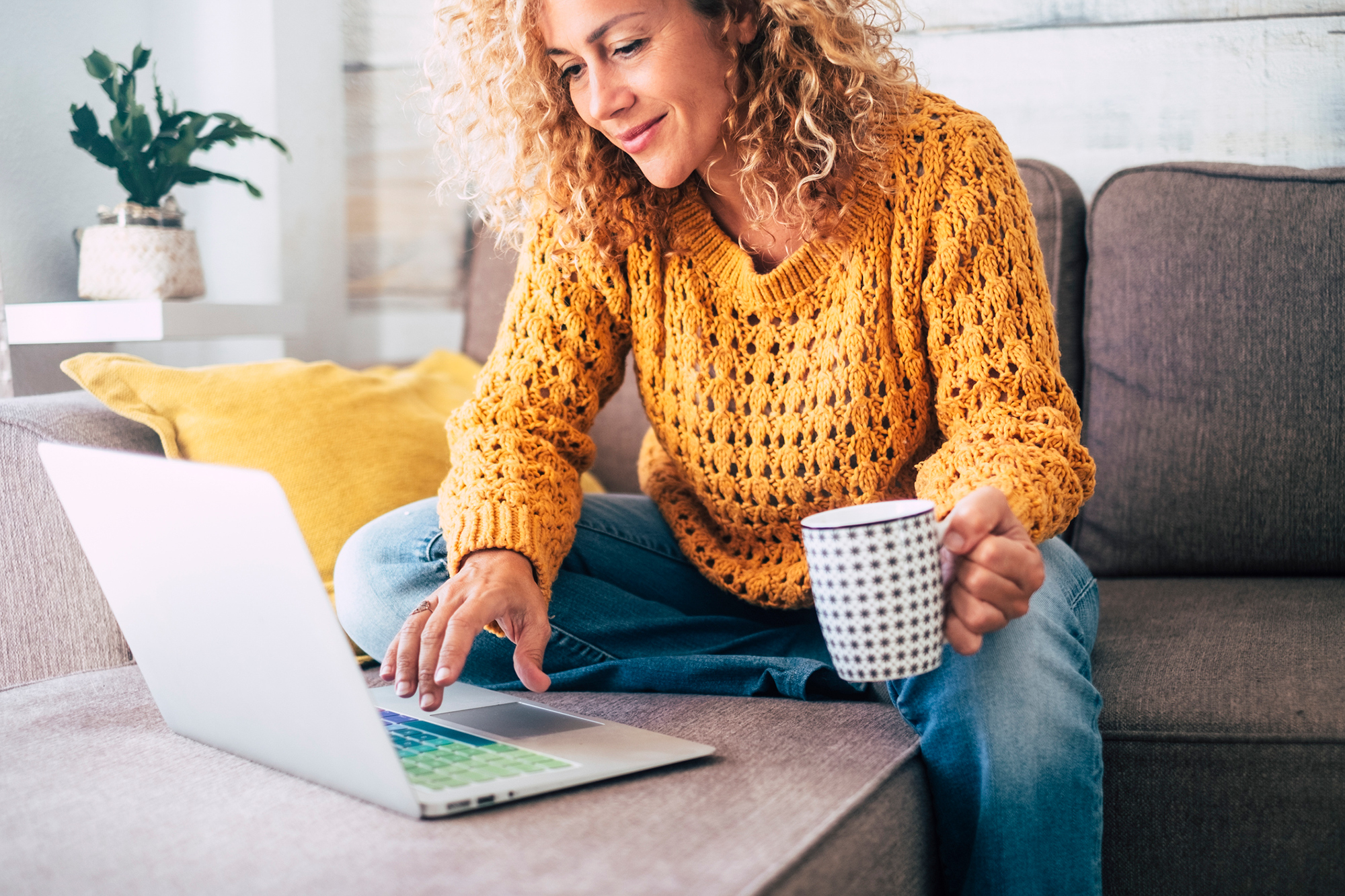 A woman looks at her laptop while holding a drink.