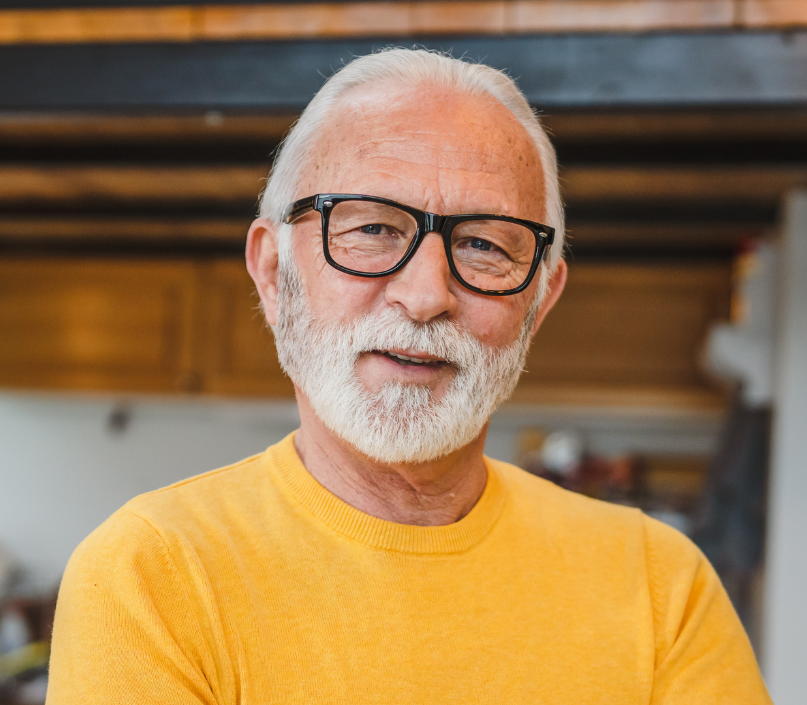 An older man in a yellow jumper looks at the camera.