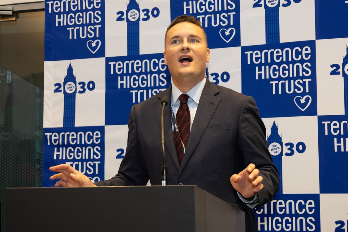 Wes Streeting stands in front a sign with Terrence Higgins Trust logos.