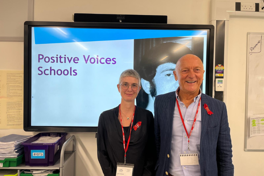 Two people stand in front of a screen at a Positive Voices school session.