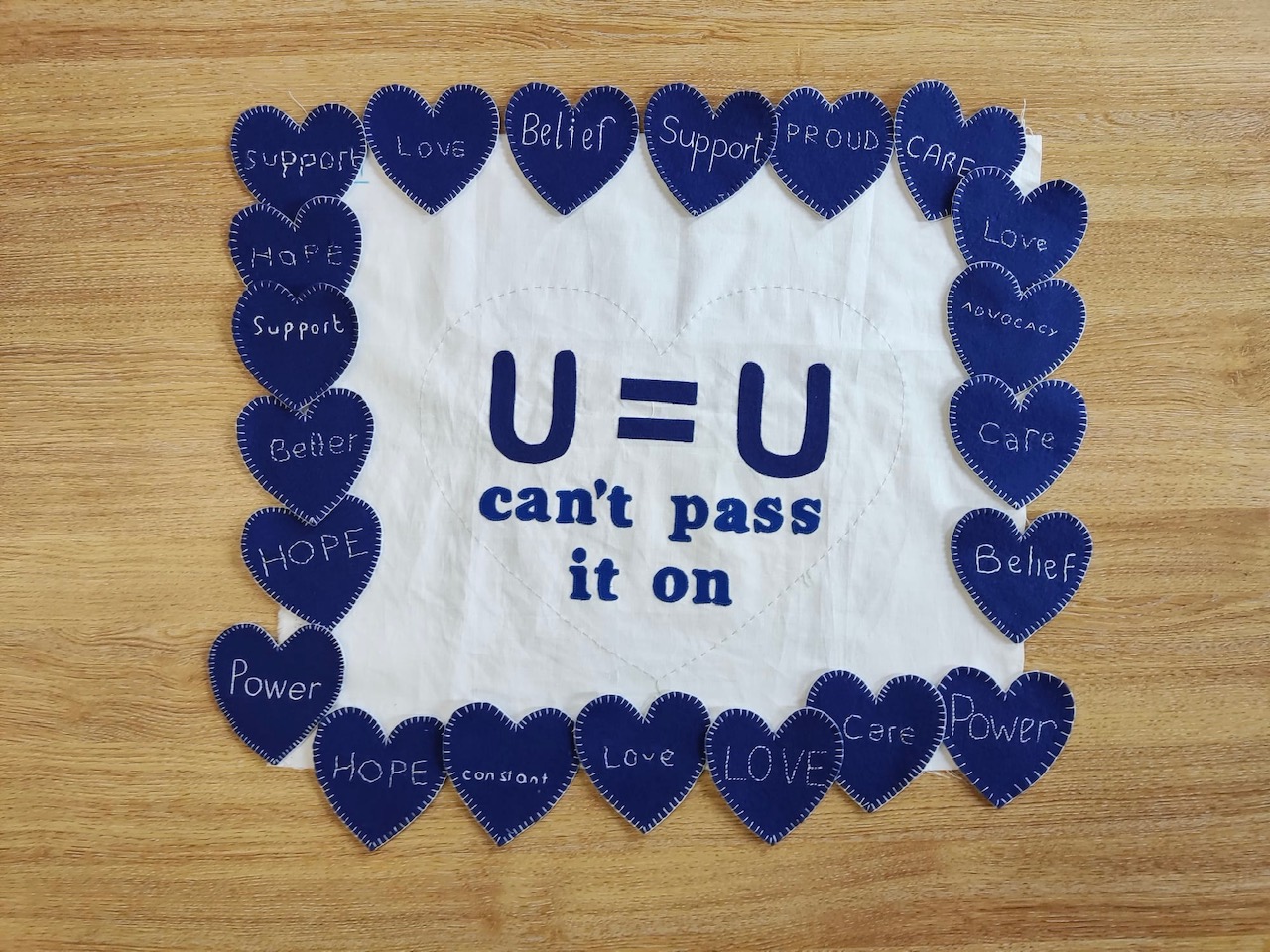 Terry Higgins AIDS Memorial Quilt panel piece reading "U=U can't pass it on" surrounded in blue hearts, photo credited to credit @handmadebygeraldine and @sarahashfordstudio 