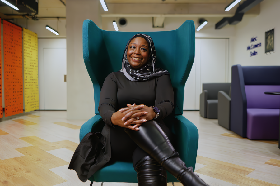 A woman sits on a teal coloured chair, smiling at the camera.