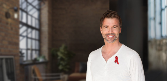 World AIDS Day A smiling white man in a white shirt with red ribbon pinned to it.