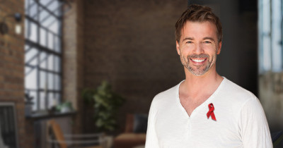 World AIDS Day A smiling man in a white shirt with a red ribbon pinned to it. The background shows a loft apartment.
