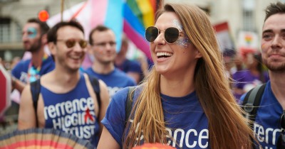 A group of people at a Pride march. They're wearing Terrence Higgins Trust blue t-shirts and carrying rainbow fans.
