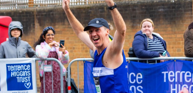 A smiling Terrence Higgins Trust London Marathon runner with his arms up.