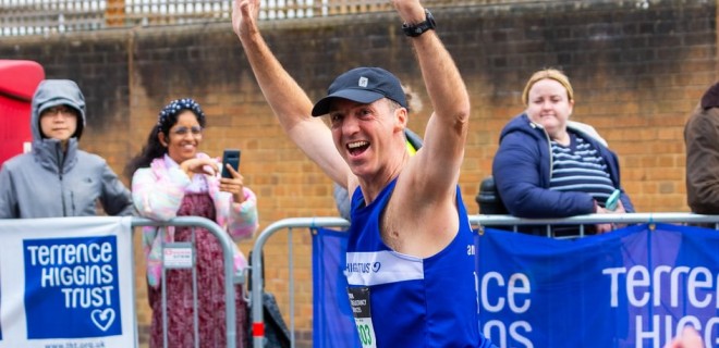 A Terrence Higgins Trust runner at the London 2024 Marathon smiling with his arms in the air.