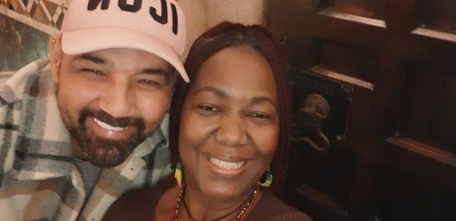 Two friends embracing. The man has his arm around the woman and they are smiling at the camera.