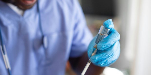 Man in a lab coat and safety goggles with a syringe.