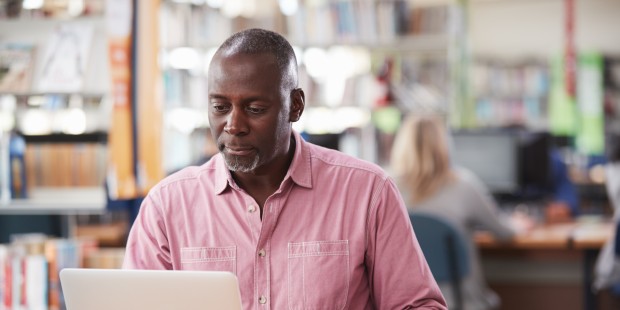 A middle aged man scrolls on his laptop.