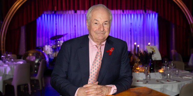 Paul Gambacini with red ribbon sat at desk at An Evening Of Radio Magic venue