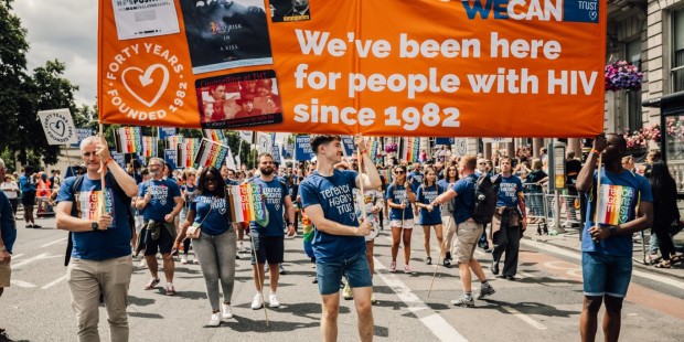 People marching for Terrence Higgins Trust at London Pride 2022. They are holding an orange banner.