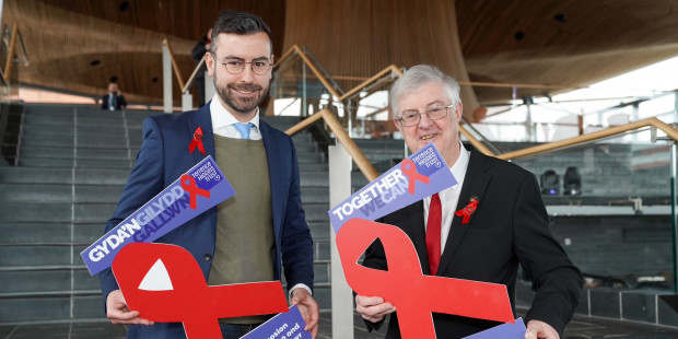 Rhys Goode and Mark Drakeford with posters saying "we can end new cases of HIV by 2030 but we need action now" in English and Welsh