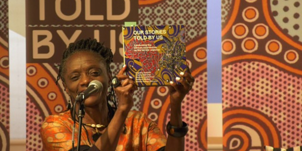 Winnie Ssanyu Sseruma holding up a copy of Our Stories Told By Us book