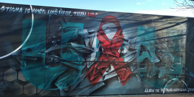 Wall mural in Dundee with red ribbon and message reading "stigma is more harmful than HIV"
