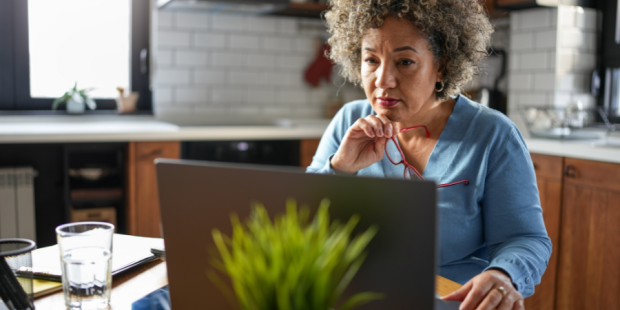 An older woman works at a laptop at a kitchen table.