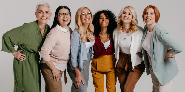 Multi-ethnic group of happy mature women bonding against grey background.